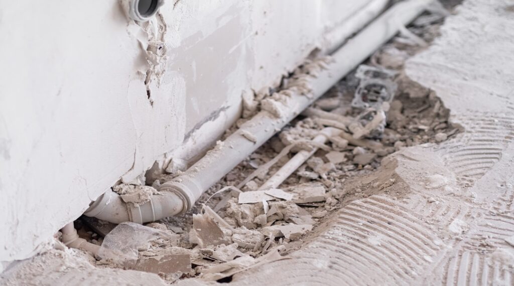 Shabby wall and drainage water pipe near hole in broken floor in bathroom